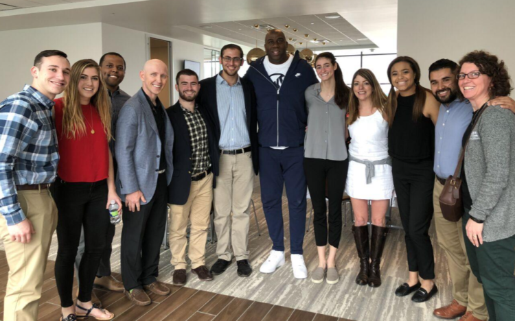 Pictured above: Earvin “Magic” Johnson, Los Angeles Lakers point guard for 13 seasons, stands with WashU students and staff at the Lakers practice facility in El Segundo, CA, on Monday, March 12, 2018. This was totally unexpected, and Magic couldn’t have been any nicer or more gracious. Michael Weisman, Taylor Cohen, Bryant Powell, Dr. Patrick Rishe, Issac Kaufer, Allan Bekerman, Magic Johnson, Kelly Minster, Teresa Iadevito, Katie Sissler, Oscar Vasco, and Konnie Henning.